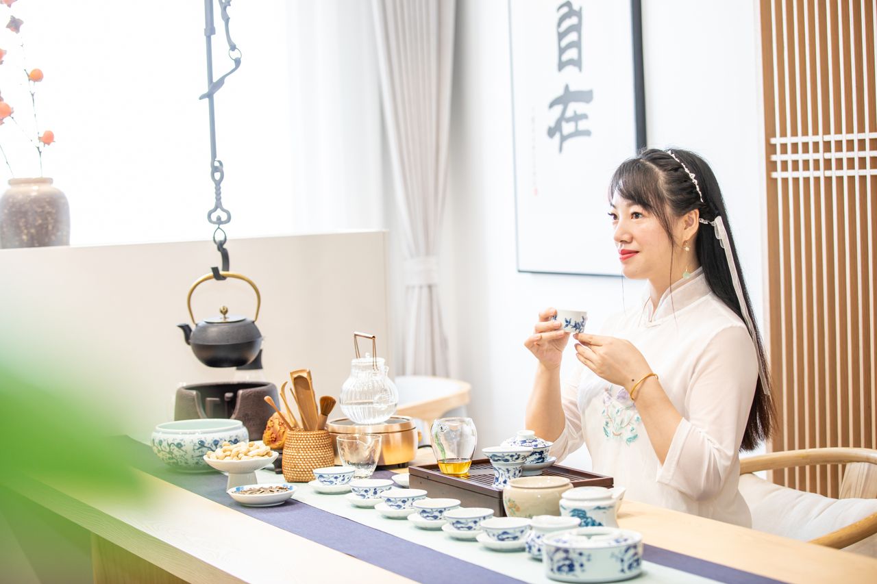 Asian woman enjoying tea ceremony in a serene, traditional setting with elegant decor.