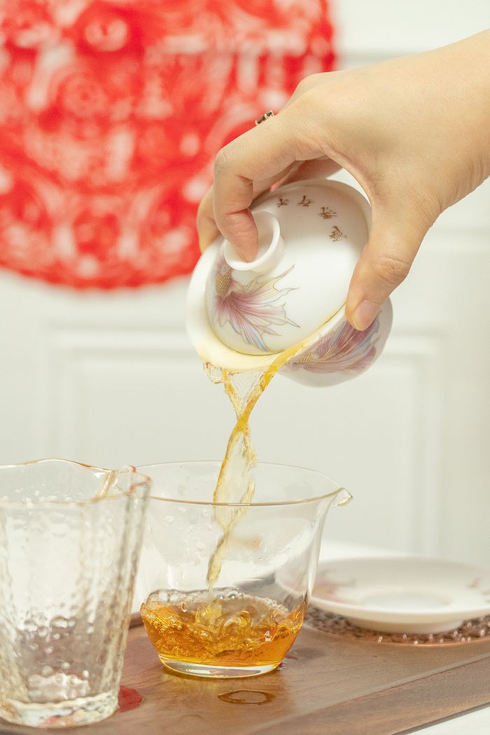 Close-up of herbal tea being poured into a glass cup from a porcelain teapot.