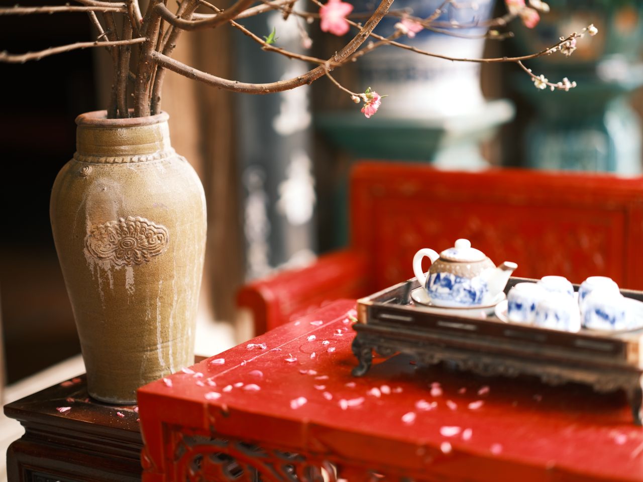 An Asian tea set on a red wooden table with a cherry blossom branch, blending tradition and tranquility.