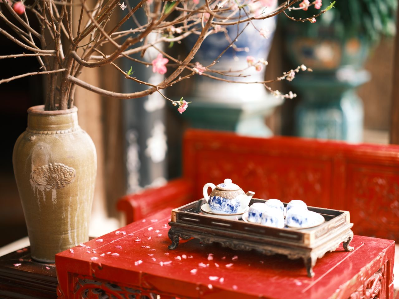 A traditional Chinese tea set with a decorative vase on a red table, accentuated by blossoming branches.